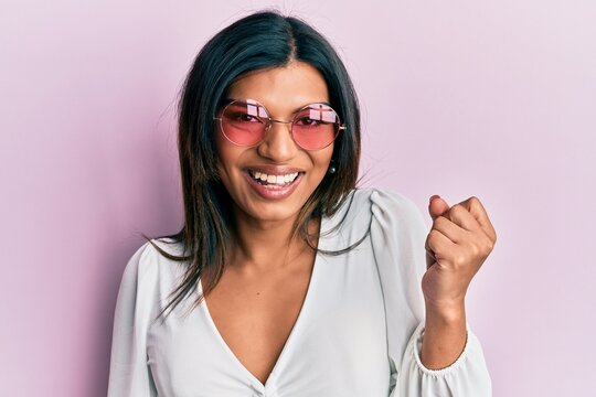 Young latin transsexual transgender woman wearing heart shaped sunglasses screaming proud, celebrating victory and success very excited with raised arm