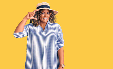 Young african american plus size woman wearing summer hat smiling and confident gesturing with hand doing small size sign with fingers looking and the camera. measure concept.