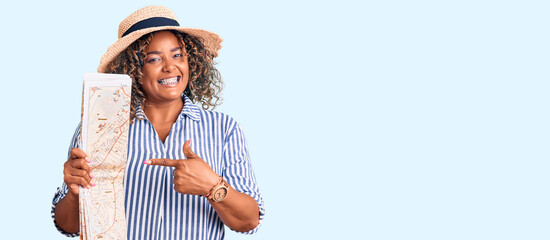 Young african american plus size woman wearing summer hat holding city map smiling happy pointing with hand and finger