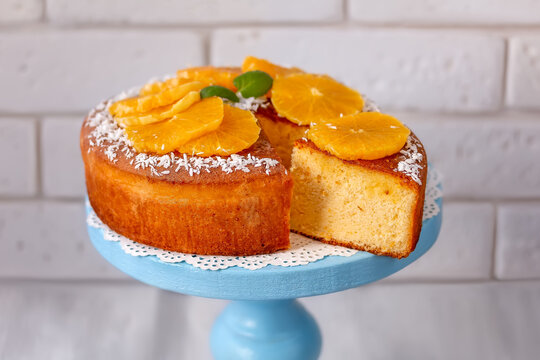 Sliced Fluffy Chiffon Cake with orange slices on cake plate. Light background, selective focus.