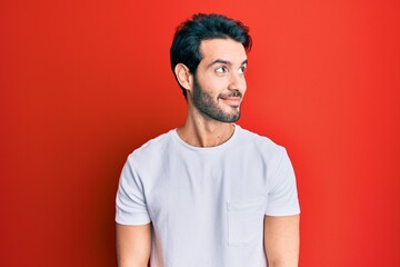 Fototapeta premium Young hispanic man wearing casual white tshirt smiling looking to the side and staring away thinking.