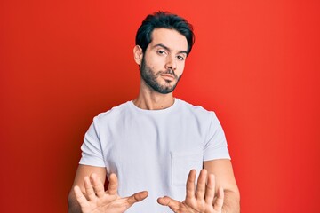Young hispanic man wearing casual white tshirt moving away hands palms showing refusal and denial with afraid and disgusting expression. stop and forbidden.