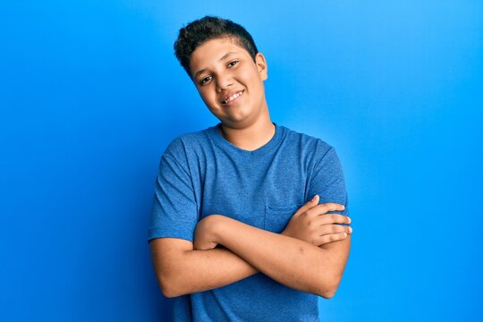 Teenager hispanic boy wearing casual blue t shirt happy face smiling with crossed arms looking at the camera. positive person.