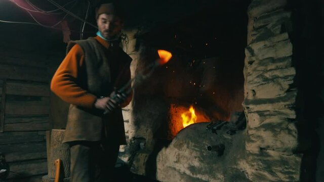 Young male blacksmith forges an ax in a smithy. Ancient hand craft culture. Preservation of historical values