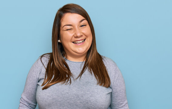 Beautiful brunette plus size woman wearing casual clothes winking looking at the camera with sexy expression, cheerful and happy face.