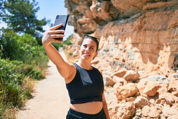 Young hispanic woman wearing sportswear smiling happy. Making selfie by the smartphone standing over beautiful landscape