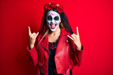 Woman wearing day of the dead costume over red shouting with crazy expression doing rock symbol with hands up. music star. heavy concept.