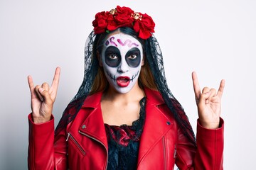 Woman wearing day of the dead costume doing rock and roll gesture with fingers in shock face, looking skeptical and sarcastic, surprised with open mouth