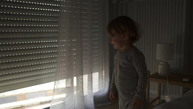 Opening automatic blinds. Little toddler child watching shades in the morning