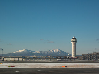 雪に覆われた恵庭岳と樽前山を背景にした新千歳空港の滑走路と管制塔