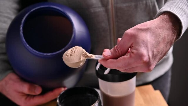 Sports nutrition supplements. Fitness, bodybuilding, healthy lifestyle concept. A man holds a chocolate whey protein powder in a measuring spoon. High quality FullHD footage