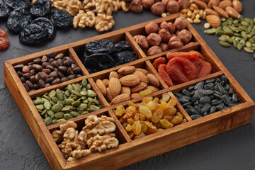 Different kinds of nuts, dried fruits  in wooden box on black slate background. Top view. Healthy food. Vegetarian nutrition