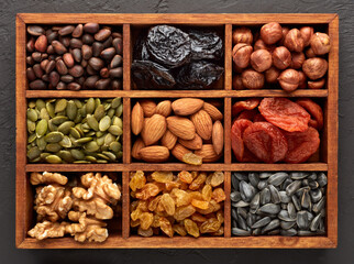 Different kinds of nuts, dried fruits  in wooden box on black slate background. Top view. Healthy food. Vegetarian nutrition