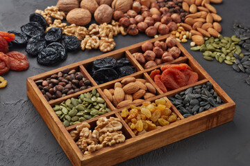 Different kinds of nuts, dried fruits  in wooden box on black slate background. Top view. Healthy...