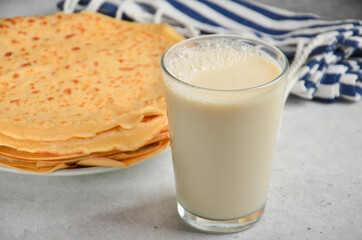 A glass of milk on a stone gray table, next to a plate of crepes.