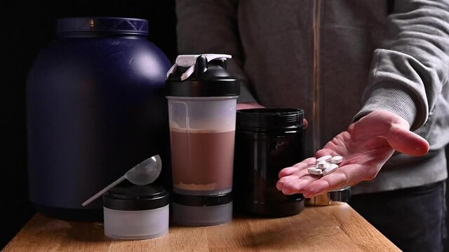 Man with sports nutrition supplements. Whey protein packaging on the table. Fitness, bodybuilding, healthy lifestyle concept. High quality FullHD footage