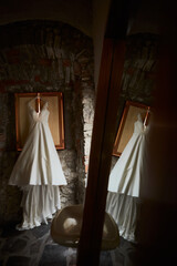 wedding dress hanging in the back of a room and which is reflected in a mirror