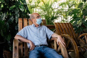 Old man sitting in rocking chair with surgical mask protecting himself from coronavirus