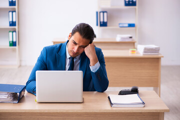 Fototapeta premium Young businessman employee unhappy with excessive work in the of