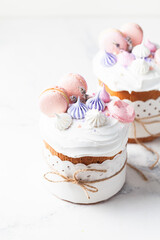 Easter cake, sweet bread decorated with white sugar icing, meringues and macaroons. Kulich wrapped in a craft paper on the white background.