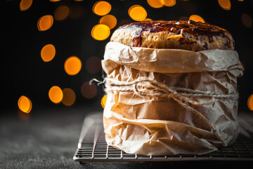 Easter cake, sweet bread. Kulich wrapped in a craft paper on the black background. Blurred bokeh lights