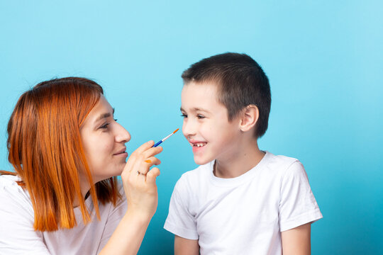 Children's creativity . Mom and son are fooling around and paints his nose with a brush on a blue background
