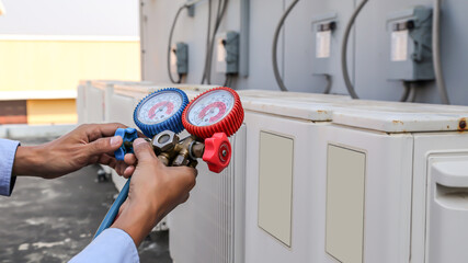 Close up hand of engineer using measuring manifold gauge for filling industrial factory air conditioners after cleaning and checking for maintenance outdoor air compressor unit.