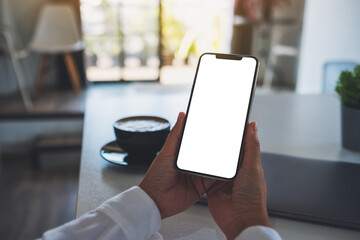 Mockup image of a woman holding mobile phone with blank white desktop screen in office