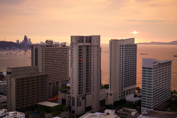 Pattaya city at chon buri in thailand on sunset or morning sunrise and warm sun light on orange sea water with boat and tower building or hotel by real estate business for holiday travel on golden sky