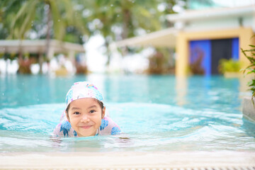 Fototapeta na wymiar Asian child cute or kid girl wearing swimming suit on edge swimming pool and smile with happy fun in water park for learn swim or refreshing and exercise on vacation summer at hotel travel or school