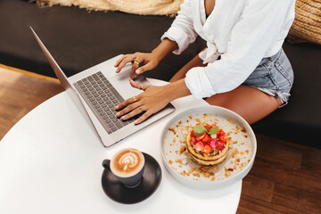 women hands at table with laptop near delicious pancakes with berries for breakfast