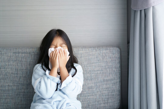 Asian child or kid girl sick and sneezing on nose with cold cough on tissue paper from influenza coronavirus and allergy weak or virus bacteria from PM 2.5 dust weather or smoke at hospital or home