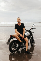 Obraz na płótnie Canvas Close up portrait of biker at beach of Bali Indonesia. Handsome man sitting on handmade vintage recast motorcycle
