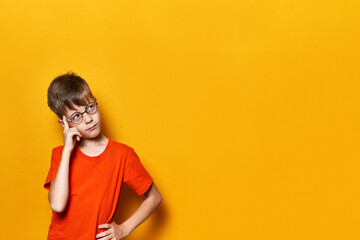 Child in thought Isolated on yellow background in orange t-shirt. Boy wearing glasses with a big...