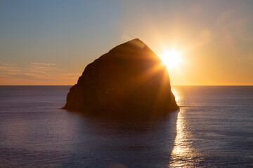 Haystack rock in silhouette, with partially clouded blue sky at sunset, along the Pacific ocean coastline, Oregon