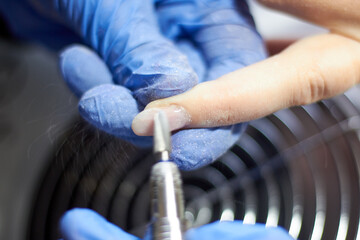 A manicurist makes a girl's nails. Sawing off old nails. Close-up - obrazy, fototapety, plakaty