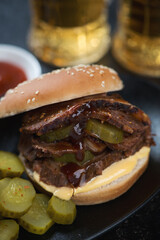 Close-up of a burger with smoked brisket and pickles, vertical shot with beer mugs in the background