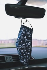 Handmade protective face mask hanging on a rear view mirror of a vehicle
