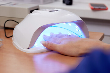 Girl dries extended nails in UV lamp, beauty salon, manicure