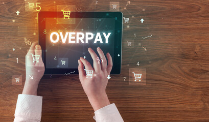Close-up of a hand holding tablet with OVERPAY inscription, online shopping concept