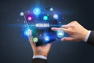 Businessman holding a foldable smartphone with WEBLOGS inscription, social media concept