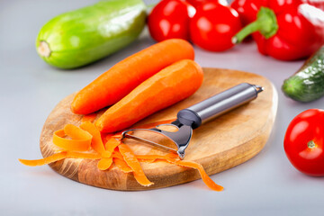  Peeling carrot for salad on chopping board. Cooking healthy meal. Fresh organic vegetables on kitchen table.