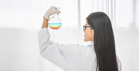 Naklejka premium Young Asian scientist woman holding and looking at the chemical flasks in the laboratory 