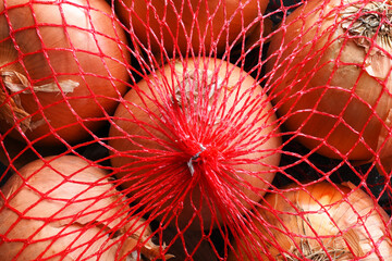 An image of several organic  yellow onion in a red mesh bag. 