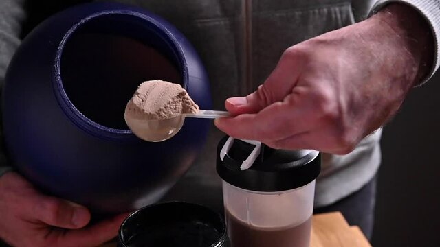 Sports nutrition supplements. Fitness, bodybuilding, healthy lifestyle concept. A man holds a chocolate whey protein powder in a measuring spoon. High quality FullHD footage