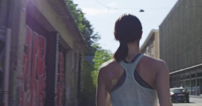 Beautiful fit athletic woman running in modern city urban environment view from behind
