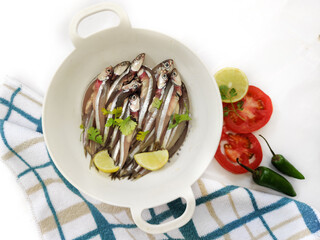 Fresh Anchovy Fish decorated with herbs and vegetables on a white background.Selective focus.