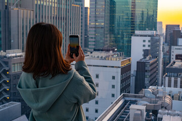 Fototapeta na wymiar 高層ビルの夕景を撮影する女性