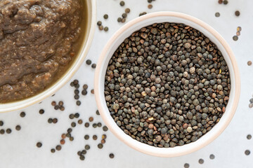 Close-up of a bowl of raw lentils with a partial view of a lentil soup dish 