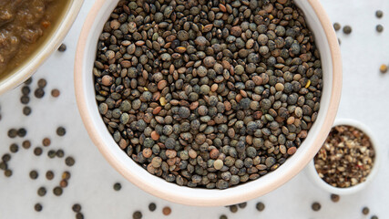 Close-up of a bowl of raw lentils with a partial view of a lentil soup dish 